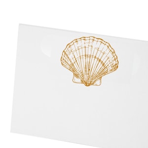 May include: A white card with a detailed, golden-brown seashell illustration. The seashell is centered and appears to be a pen and ink drawing. The card is angled, showing a corner.