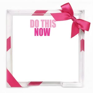 May include: A square clear acrylic memo holder featuring a white notepad with the text DO THIS NOW printed in bold pink letters. The holder is accented with a bright pink satin ribbon tied into a bow at the top right corner of the frame.