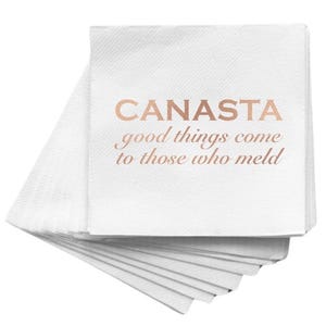 May include: A stack of white paper napkins with the word "CANASTA" printed in a copper color, along with the phrase "good things come to those who meld". The napkins are stacked at an angle.