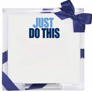 May include: A square, clear acrylic holder containing a stack of white paper sheets. The text "JUST DO THIS" is printed in light blue and dark blue on the top sheet. A dark blue satin ribbon is tied around the corner of the acrylic holder.