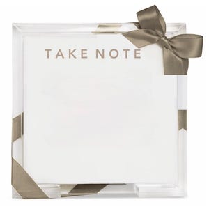 May include: A square clear acrylic holder containing a stack of white paper sheets. The text TAKE NOTE is printed in a neutral tone at the top. A taupe-colored satin ribbon is wrapped around the acrylic frame and tied in a bow at the top right corner.