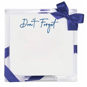 May include: A square clear acrylic memo holder containing a stack of white paper sheets. The text "Don't Forget" is printed in dark blue script on the top sheet. A dark blue satin ribbon is tied in a bow at the top right corner of the holder.