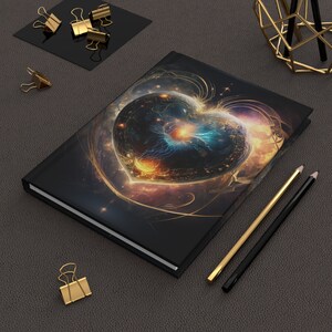 May include: A black notebook with a colorful, abstract heart design. The heart is made up of swirling colors and textures, including blue, yellow, orange, and white. The notebook is closed and lying on a dark surface.