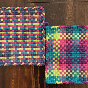May include: Two colorful, woven potholders. One is rectangular, the other square. Both feature a vibrant pattern of turquoise, pink, purple, and yellow. Each has a purple loop for hanging. The potholders are handmade and suitable for kitchen use.