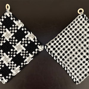 May include: Two woven potholders. One features a black, white, and gray houndstooth pattern, and the other has a black and white gingham design. Both have a loop for hanging and a scalloped edge.