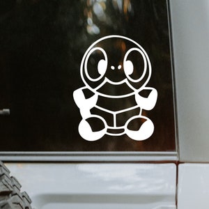 May include: White vinyl sticker of a cartoon turtle with big eyes and a shell. The sticker is on the back window of a car.