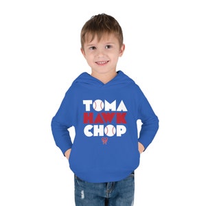 May include: A royal blue hooded sweatshirt with the words "Tomahawk Chop" in white letters with red accents and a baseball graphic. The sweatshirt has a small red tomahawk logo at the bottom.