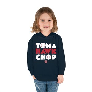 May include: A navy blue hooded sweatshirt with the words "Tomahawk Chop" in white letters with red baseballs in the letters. The logo of the Atlanta Braves is on the bottom of the sweatshirt.