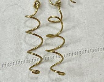 May include: A pair of gold-colored spiral earrings. Each earring features a hook and a coiled wire design, creating a spring-like appearance. The earrings are displayed on a white, textured surface.