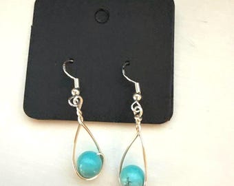 May include: A pair of silver dangle earrings with turquoise beads. The earrings are in the shape of a teardrop.