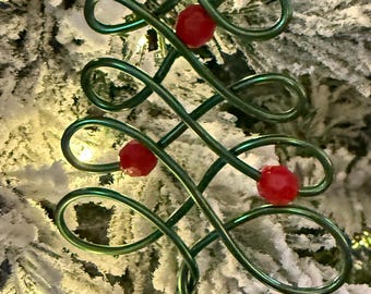 May include: A green wire Christmas tree ornament with red beads. The ornament is hanging on a snowy Christmas tree.