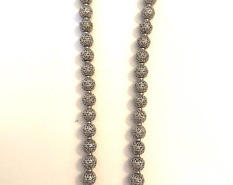 May include: A silver-colored necklace featuring a series of intricately designed, hollow, spherical beads. The beads are strung together, creating a long, elegant necklace. The necklace is displayed against a white background.
