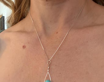 May include: A silver necklace with a teardrop pendant. The pendant features a light blue, round stone encased in a silver wire frame. The chain is a delicate silver box chain.