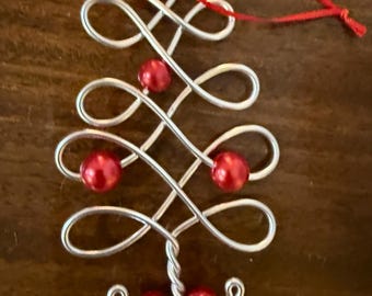 May include: A silver wire Christmas tree ornament with red beads. The ornament has a red string for hanging.
