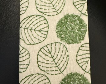 May include: A white fabric notebook cover with a green leaf pattern embroidered on it.
