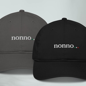 May include: Two baseball caps, one gray and one black, with the word "nonno" embroidered on the front. The black cap has a small Italian flag embroidered next to the word.