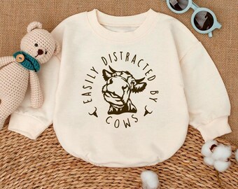 May include: A cream colored long-sleeved shirt with a brown graphic of a cow's head and the text "Easily Distracted By Cows" in a circle.
