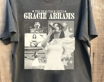 Puede incluir: Camiseta negra con un estampado blanco de Gracie Abrams, el texto "The Eras Tour 2023" y varias estrellas. El estampado presenta cuatro imágenes de Abrams actuando en el escenario.