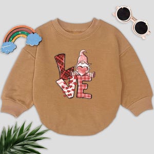 May include: A brown sweatshirt with a graphic of a gnome holding a heart and the word "LOVE" in patchwork letters.