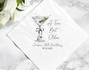 May include: White cocktail napkin with a martini glass illustration. The glass contains olives and is decorated with a black bow and green ribbon. Text reads "A Tini Bit Older" and "Jennifer's 30th Birthday 09.10.2025".