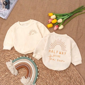 May include: Two cream colored long-sleeved shirts with a sun graphic. One shirt says "Halfway Around the Sun" and the other says "Sophia".