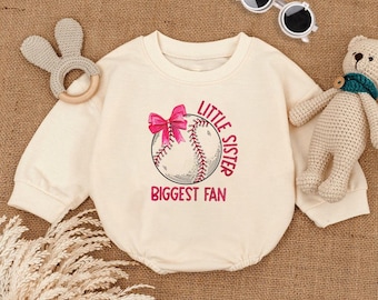 Peut inclure: Combinaison bébé crème avec un motif de baseball et le texte "Little Sister Biggest Fan" en rose. La combinaison a des manches longues et un col rond. Un nœud rose est sur le motif de baseball. Accessoires pour bébés.
