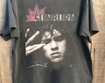 May include: A black t-shirt with a faded image of a man with a crown and the word "SUNBURN" printed on it. The man's signature is visible below the image.