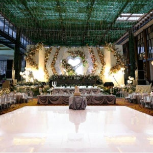 Pu&ograve; includere: Un pavimento da ballo bianco con un grande palco decorato sullo sfondo. Il palco &egrave; adornato con fiori bianchi e dorati, vegetazione e una grande struttura a forma di cuore. Il pavimento da ballo &egrave; illuminato da faretti.