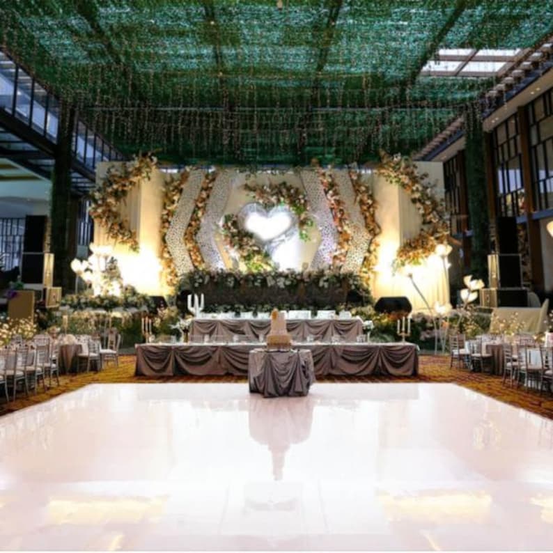 Pu&ograve; includere: Un pavimento da ballo bianco con un grande palco decorato sullo sfondo. Il palco &egrave; adornato con fiori bianchi e dorati, vegetazione e una grande struttura a forma di cuore. Il pavimento da ballo &egrave; illuminato da faretti.