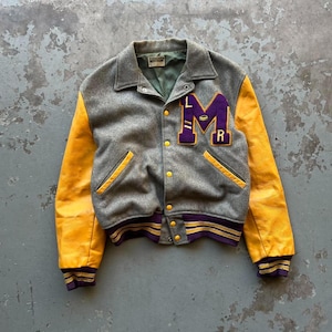 May include: A vintage letterman jacket in gray wool with bright yellow leather sleeves. The jacket features a purple and gold "LMR" patch on the chest, yellow buttons, and striped purple and gold cuffs and waistband.
