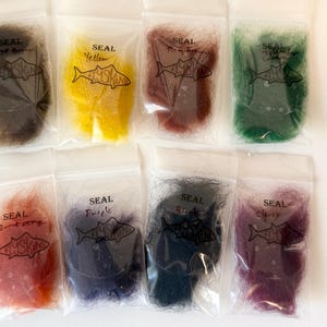 May include: Nine small plastic bags filled with colorful craft materials. Each bag is labeled with a color name and a fish illustration. Colors include brown, yellow, red, purple, black, and green. The bags are arranged on a white surface.