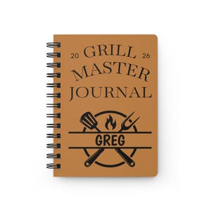 Peut inclure: Un carnet à spirales marron avec la mention "GRILL MASTER JOURNAL" et le nom "GREG" sur la couverture. La couverture présente également un dessin d'ustensiles de cuisine. Le carnet est destiné aux amateurs de grillades.