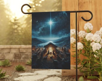 Può includere: Una bandiera da giardino natalizia con un cielo notturno blu, una stella brillante e una scena della Natività con una mangiatoia, Maria, Giuseppe e il bambino Gesù. La scena è circondata da pecore e pastori.