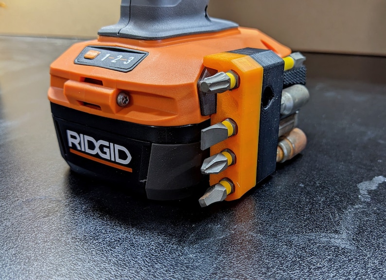Puede incluir: Una herramienta el&eacute;ctrica Ridgid negra y naranja con un porta-puntas negro y naranja fijado en el lateral. El porta-puntas tiene seis puntas diferentes con puntas amarillas.