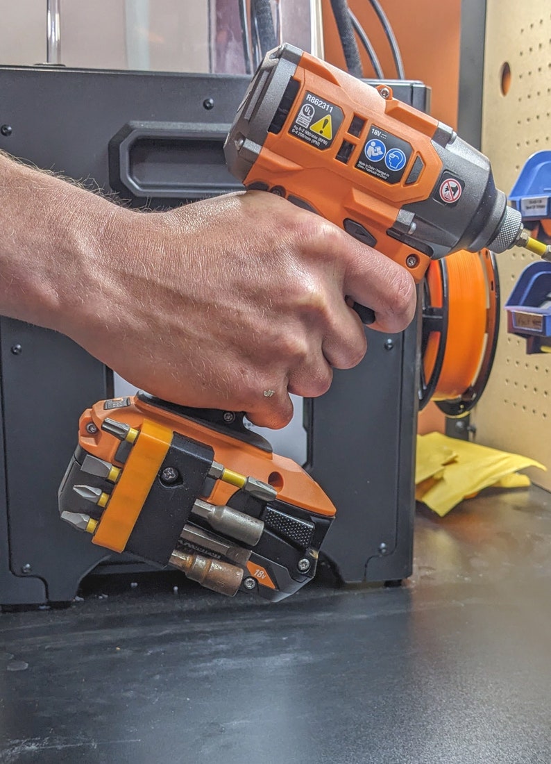 Puede incluir: Un taladro inal&aacute;mbrico naranja y negro con una bater&iacute;a de 18V y un accesorio de destornillador multi-bits. El taladro est&aacute; en la mano de una persona.