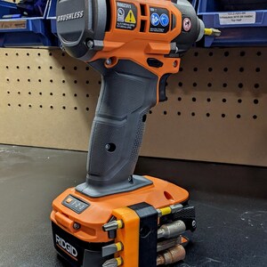 Puede incluir: Un taladro inal&aacute;mbrico negro y naranja con motor sin escobillas y una bater&iacute;a. El taladro tiene un ajuste 1-2-3 en la bater&iacute;a y un soporte de brocas en el lateral. El taladro est&aacute; etiquetado como "RIDGID" y "BRUSHLESS".