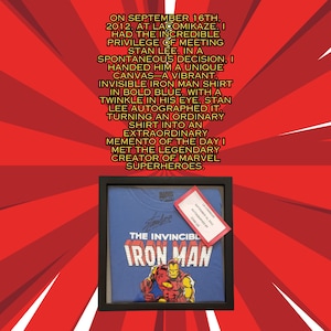 Op de afbeelding: Een ingelijst blauw T-shirt met een rode en gele Iron Man-afbeelding en de tekst "The Invincible Iron Man". Het shirt is gesigneerd door Stan Lee met de datum 16 september 2012.