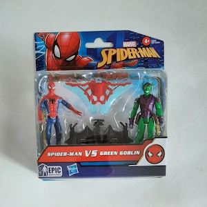 May include: A packaged Spider-Man vs. Green Goblin action figure set. The figures are in a clear plastic case with a cardboard backing featuring the Marvel Spider-Man logo and the text "Spider-Man vs Green Goblin". The figures are red, blue, and green.