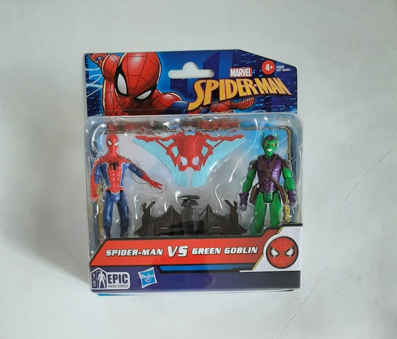 May include: A packaged Spider-Man vs. Green Goblin action figure set. The figures are in a clear plastic case with a cardboard backing featuring the Marvel Spider-Man logo and the text "Spider-Man vs Green Goblin". The figures are red, blue, and green.