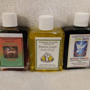 May include: Three glass bottles with white lids, each holding a different coloured liquid. The bottles have labels with text in Spanish and English, including "Scented Oil" and "Calm Balm".
