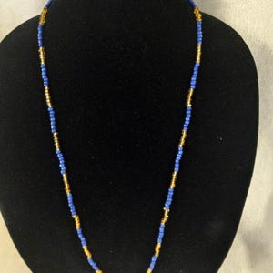 Puede incluir: Un collar de cuentas azules y doradas en un maniquí negro.