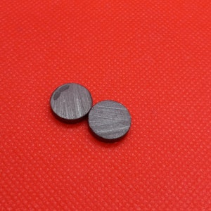 Puede incluir: Dos discos redondos, negros y metálicos sobre una superficie roja texturizada.