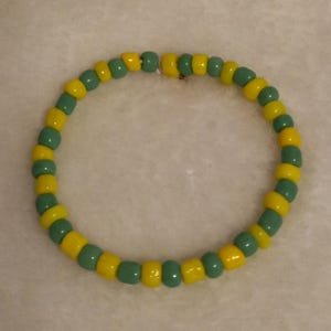 Può includere: Un braccialetto di perline con perline gialle e turchesi alternate. Le perline cilindriche sono infilate per formare un cerchio. Un accessorio semplice e colorato, composto da perline spaziate uniformemente.