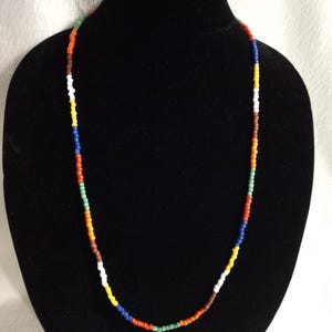 Peut inclure: Un collier de perles multicolores avec des perles alternées de blanc, orange, rouge, vert, bleu et marron.