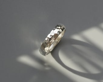 May include: A silver hammered band ring. The ring is smooth and shiny, with a textured surface.