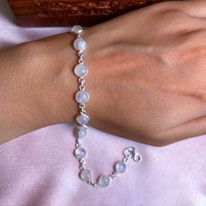 May include: A silver bracelet with a chain and round moonstone beads. The bracelet is on a person's wrist.