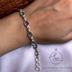 May include: A silver bracelet with a chain and teardrop-shaped iridescent gemstones. The bracelet has a lobster clasp closure.