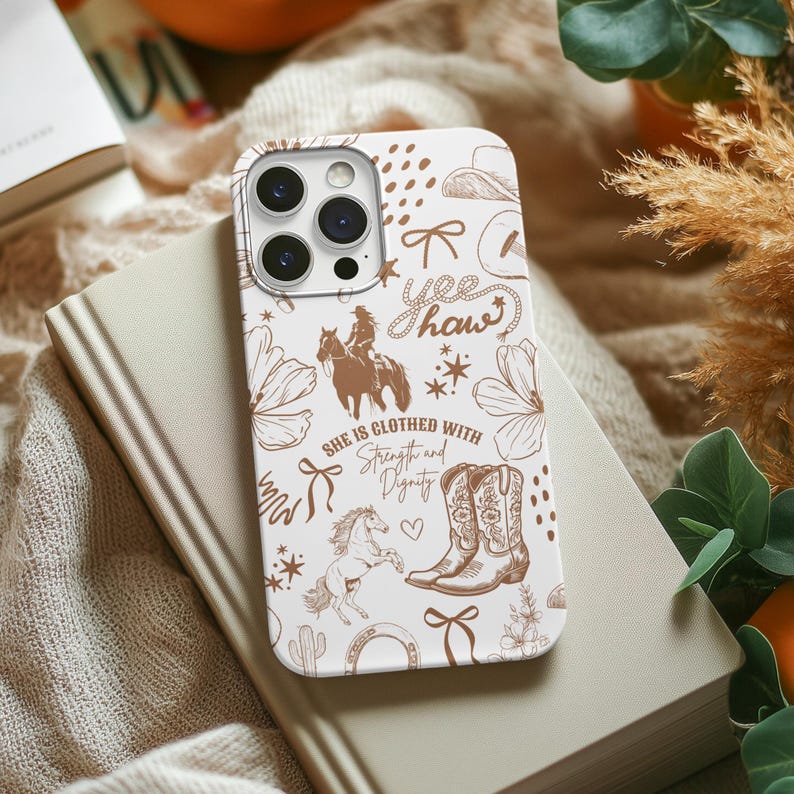 May include: White iPhone case with a brown and white design. The design features a horse, cowboy boots, a horseshoe, and the text "Yee Haw" and "She is clothed with strength and dignity".