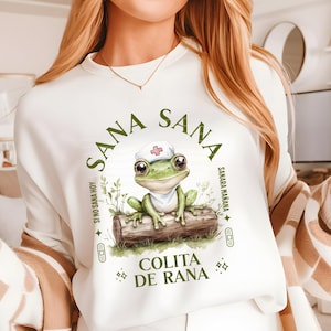 natural color shirt with a cute frog sitting on a log and wearing a nurse hat and the phrase: Sana Sana Colita de Rana
