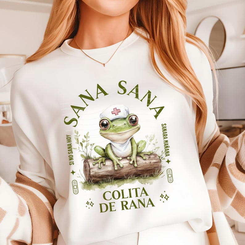 natural color shirt with a cute frog sitting on a log and wearing a nurse hat and the phrase: Sana Sana Colita de Rana